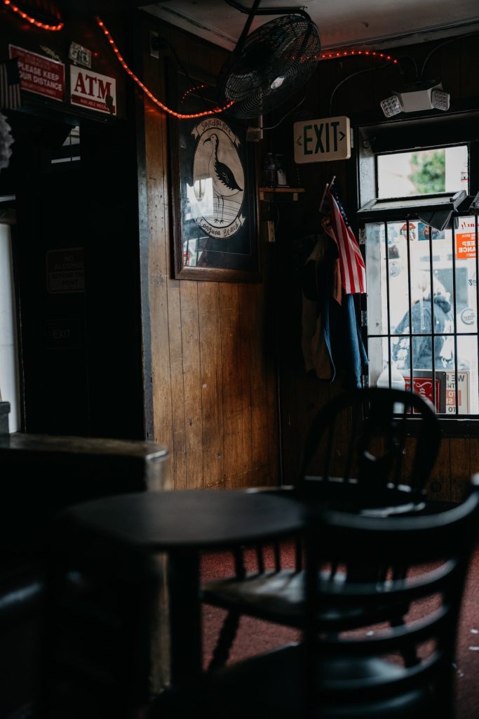 Tables and chairs inside the Sandpiper Lounge, wood paneling, and the exit sign by the door